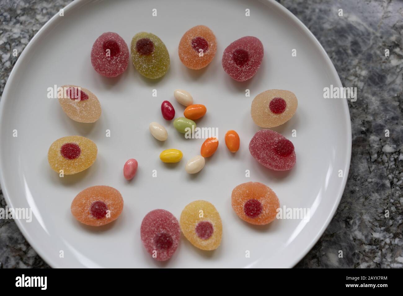 Easter candies in a circle on a white plate on a gray granite table. Concept, High angle view, space for text. Stock Photo