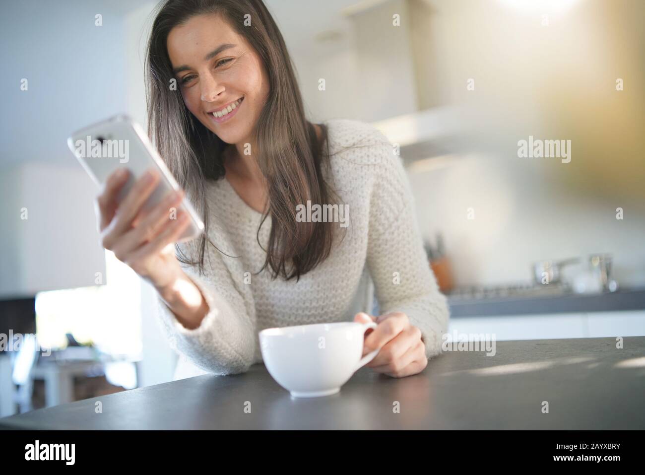 Relaxed beautiful brunette texting in modern kitchen Stock Photo