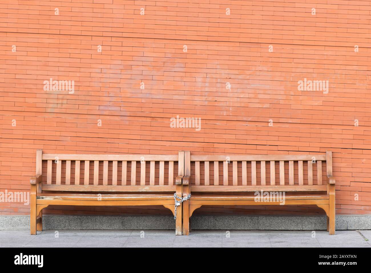 Two chained wooden benches in front of a brick wall. Stain in the wall ...