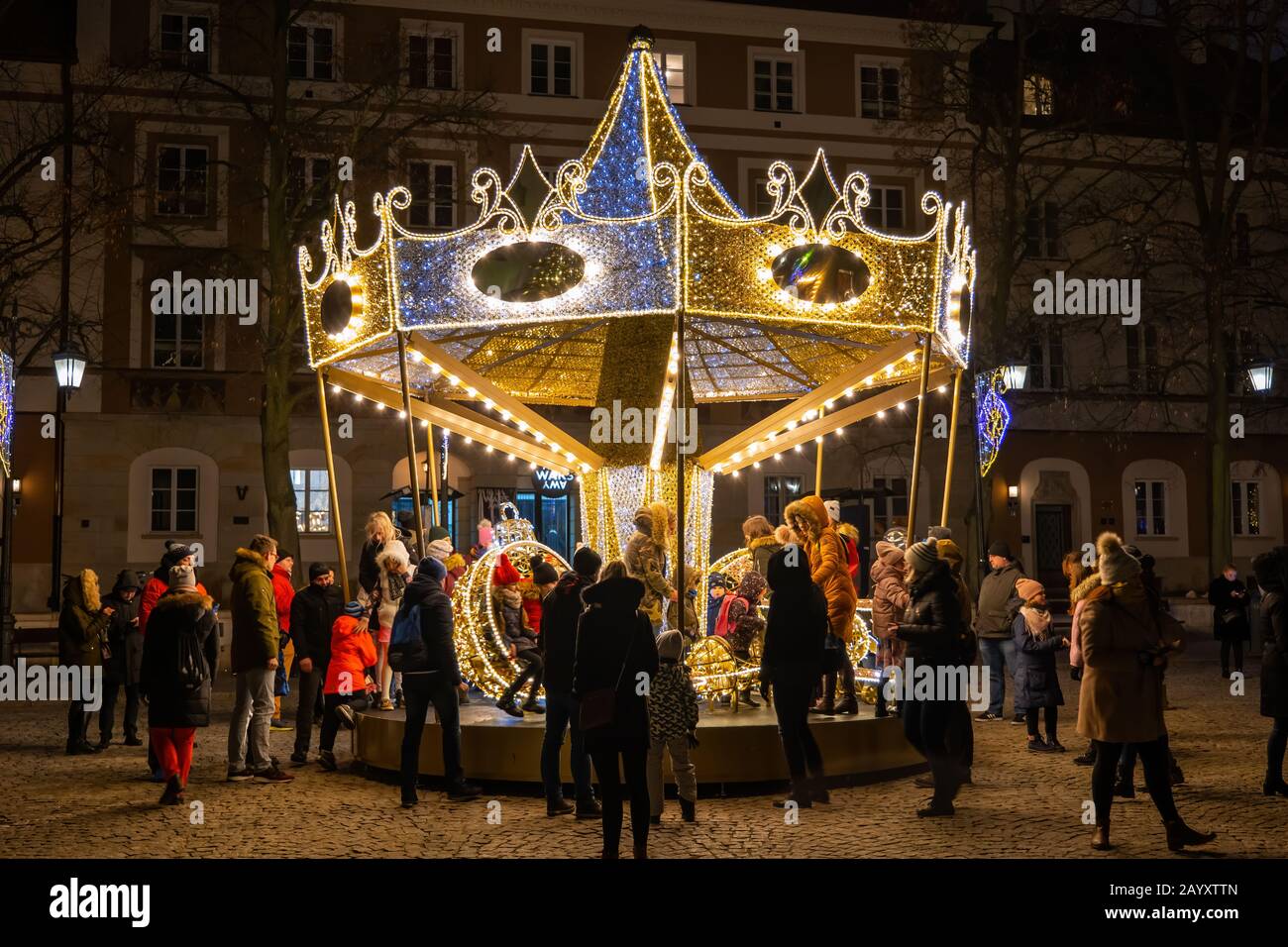 Warsaw, Poland - December 27, 2019: People with children having fun at carousel roundabout amusement ride at night during Christmas holiday season on Stock Photo
