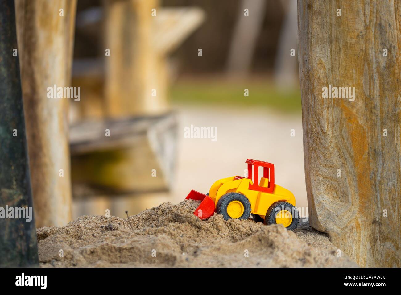 yellow digger with shovel for children standing in the sand of a playground for kids. Stock Photo