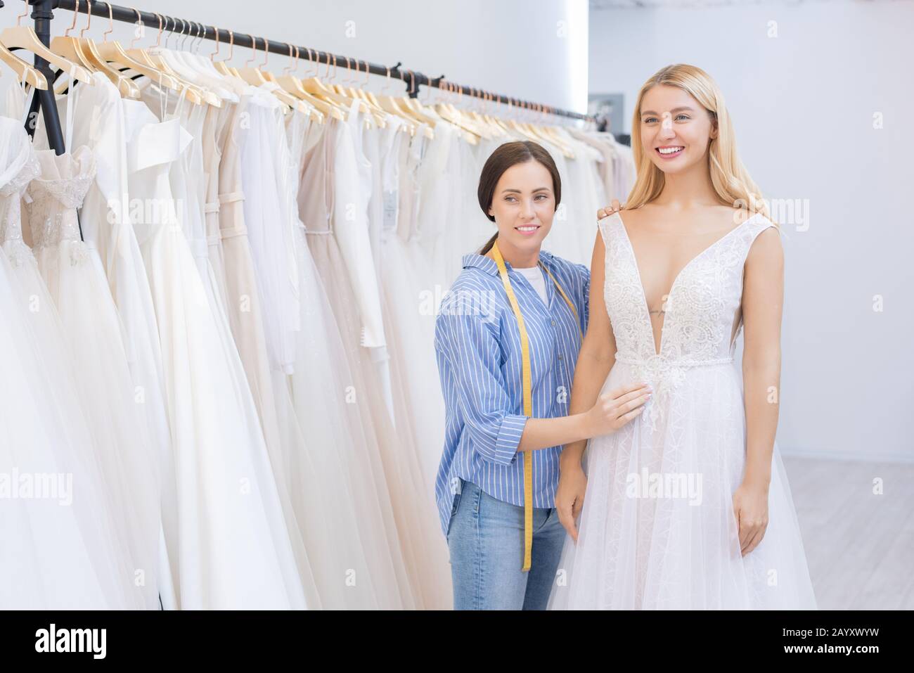 Attractive Young Woman Trying On Wedding Dress In Modern Bridal Shop Sales Assistant Helping 4570