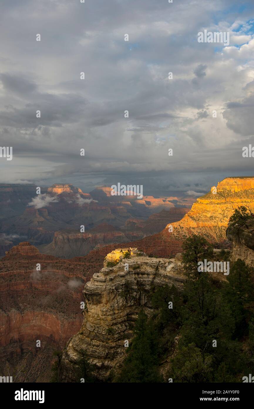 People on a rock outcrop between Yavapai Point and Mather Point on the South Rim of the Grand Canyon with clearing clouds after a thunderstorm in the Stock Photo