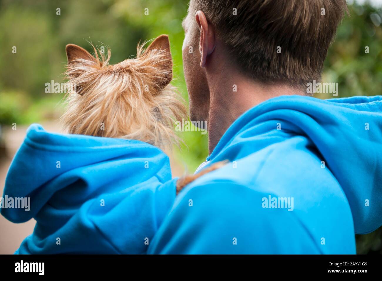 Dog and owner in matching blue hoodies standing outdoors in bright