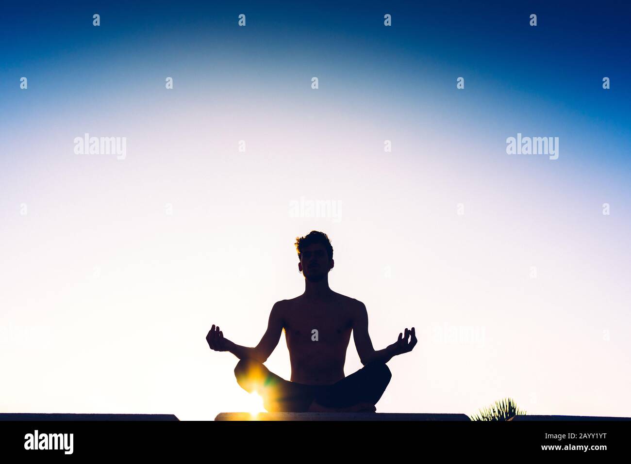 Silhouette of a man practicing the yoga lotus pose with the sun behind ...