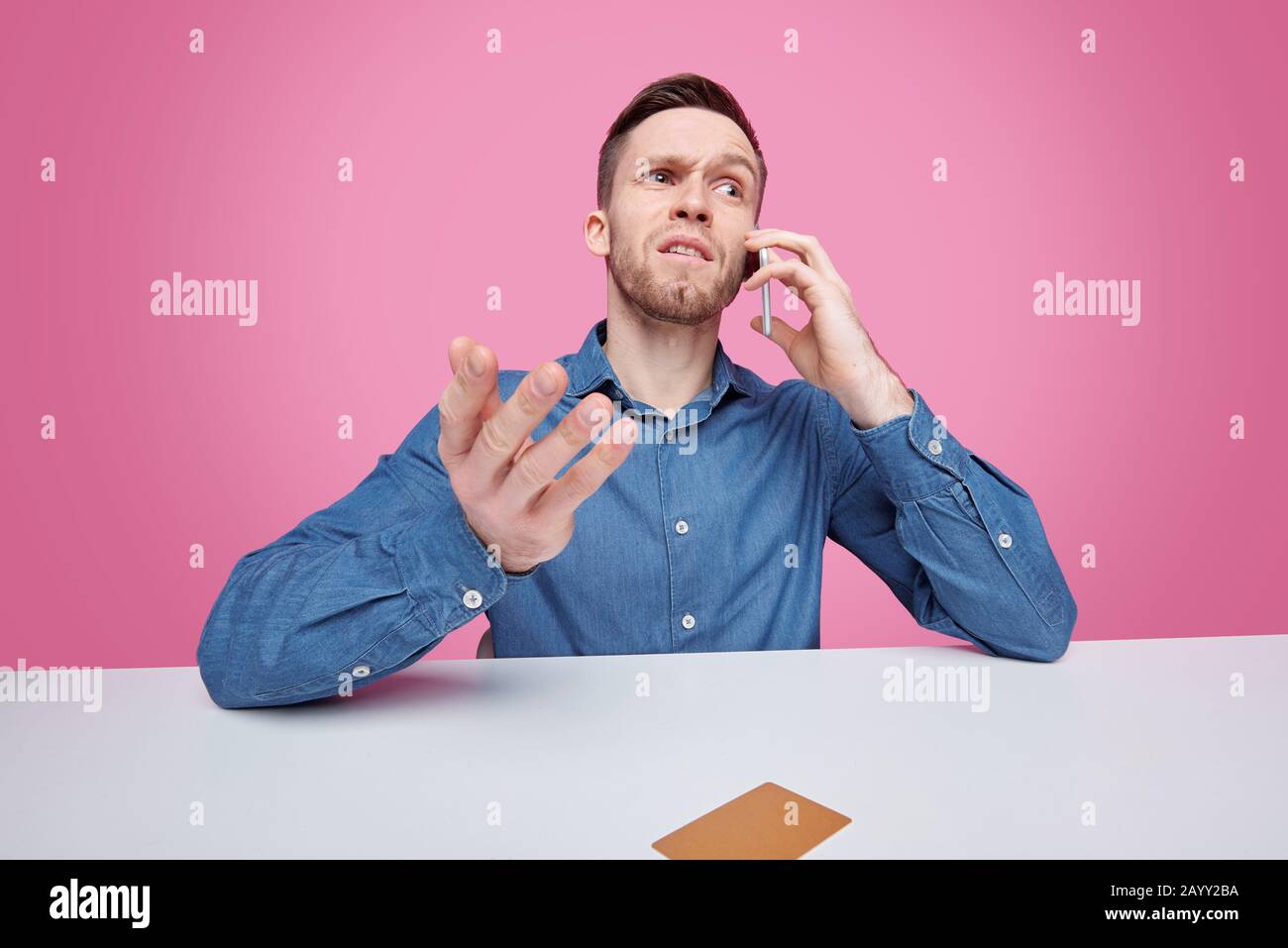 Serious young man in jacket sitting at table and solving cube puzzle while developing logic Stock Photo