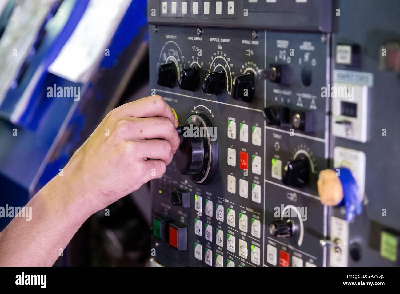 Operator hand spinning jog handle on CNC machine control panel. Close-up with selective focus and blur. Stock Photo