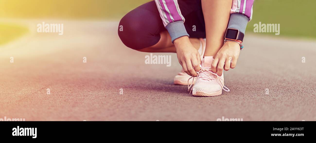 Modern sporty female runner tying shoelaces before going for a run in park Stock Photo