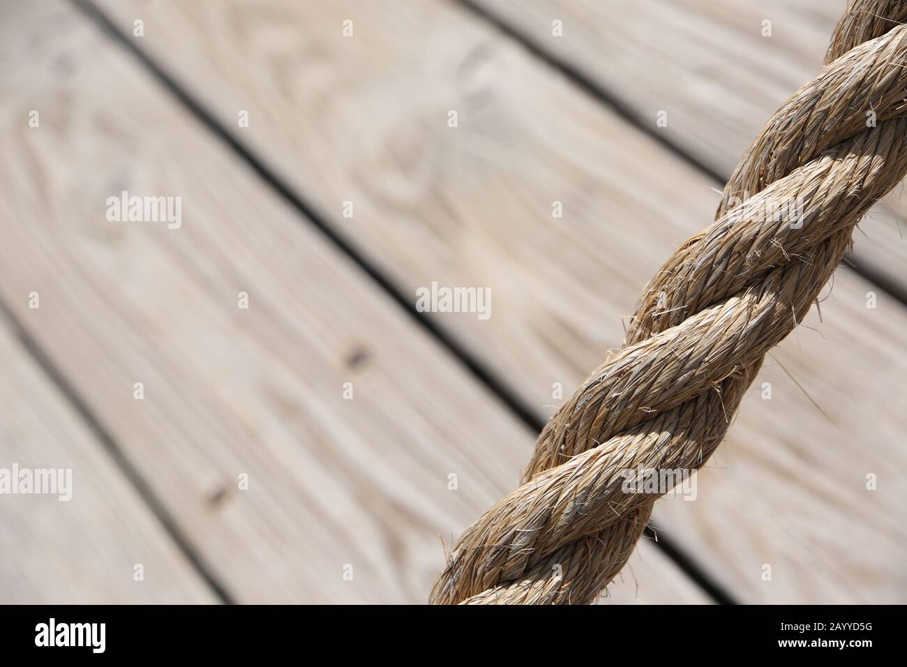 Aged rope with wooden floor boards in the background creating a natural aged texture for use as a background. Stock Photo
