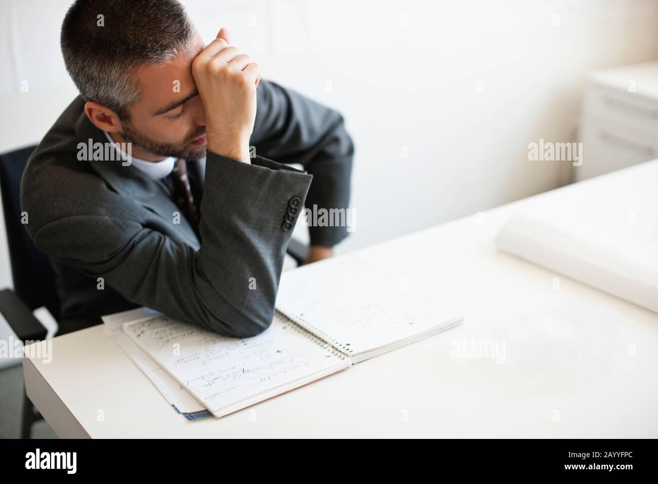 Businessman sits looking stressed with hand to face. Stock Photo