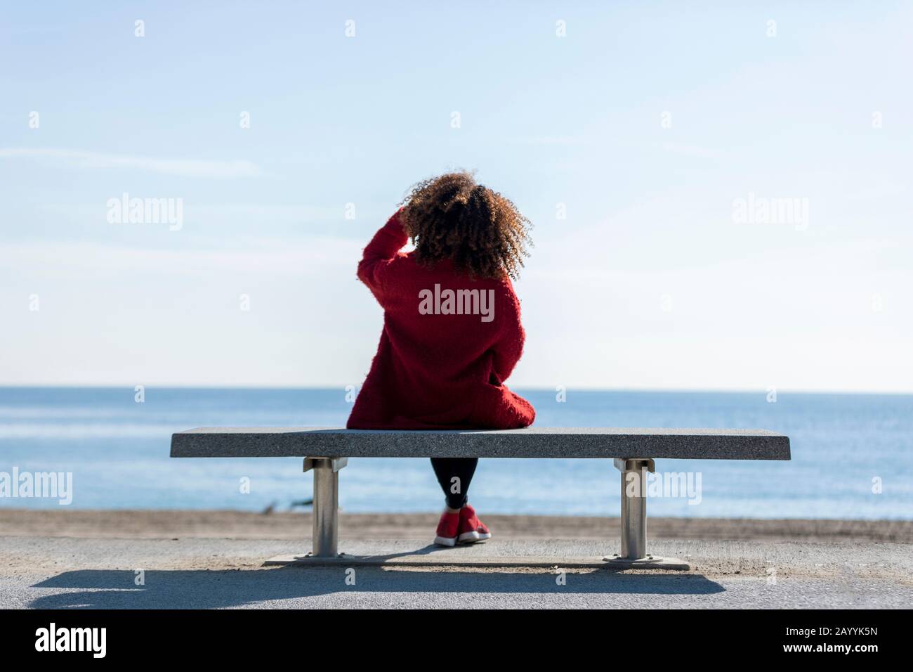 Rear view of a young curly woman wearing red denim jacket sitting on a
