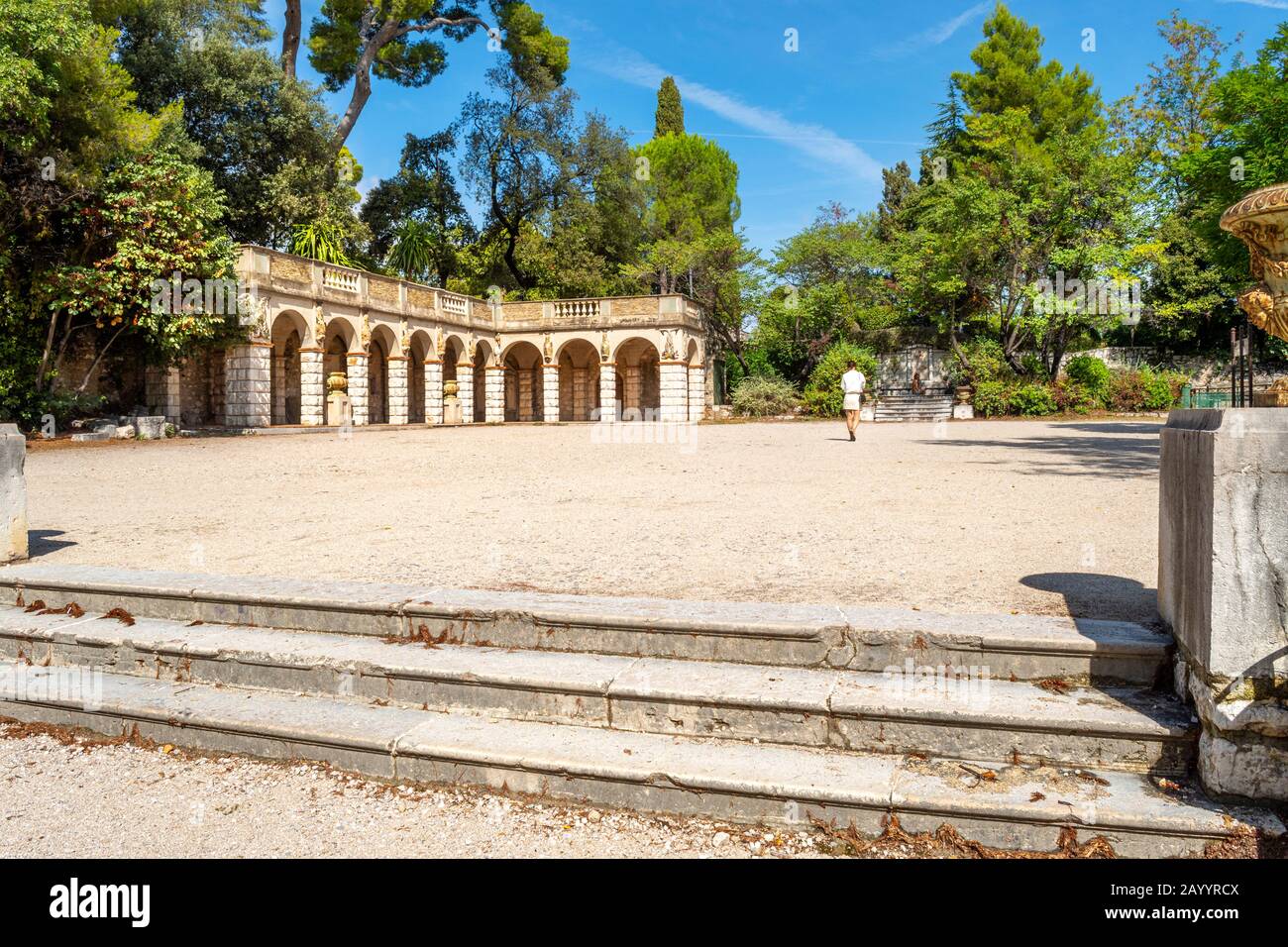 A solo female traveler walks through a gravel courtyard near an arched Roman building on Castle Hill in Nice, France. Stock Photo