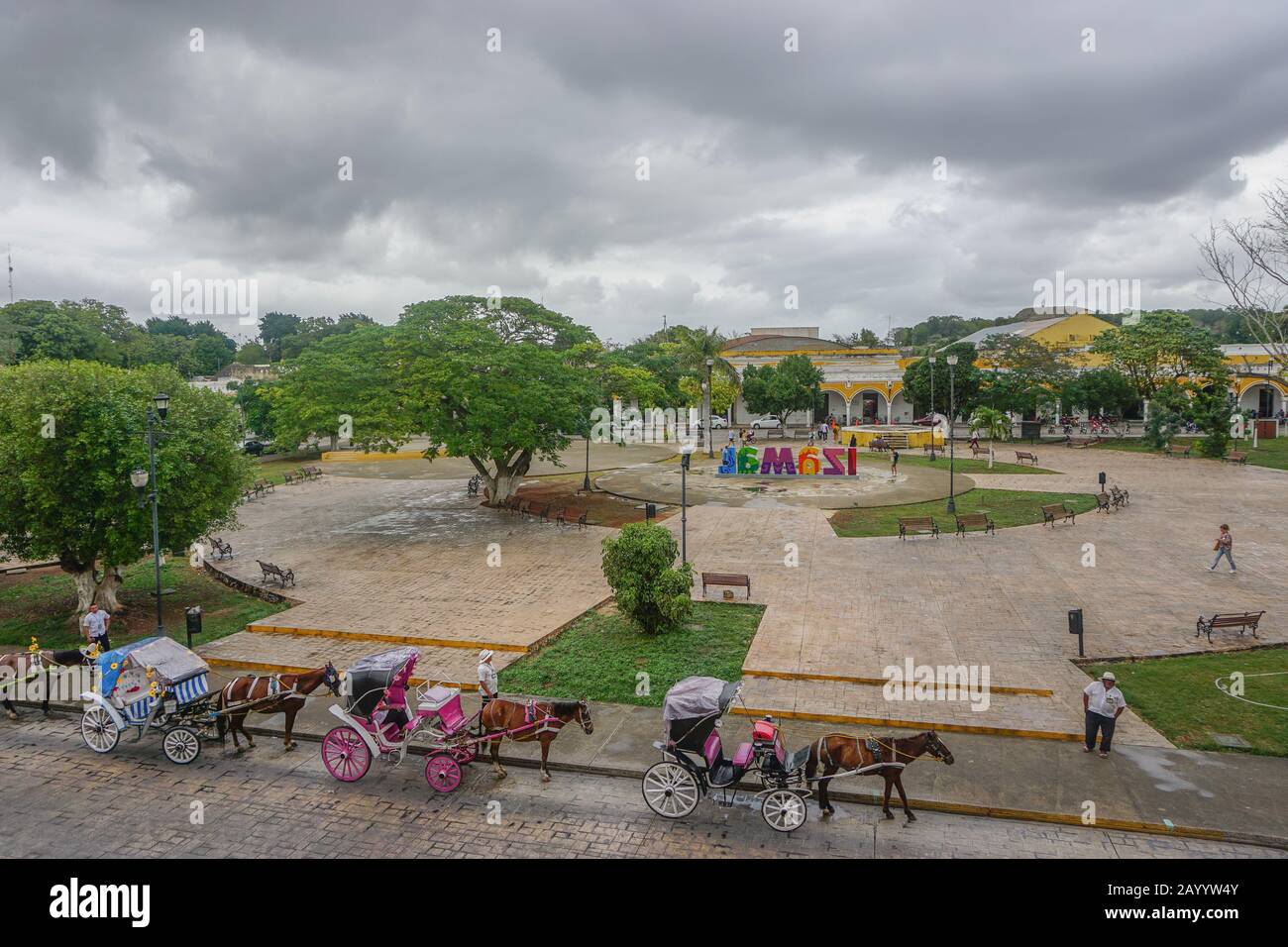 Izamal, Yucatan, Mexico: Horses and carriages wait for passengers along the main plaza of Izamal, under a cloudy sky. Stock Photo