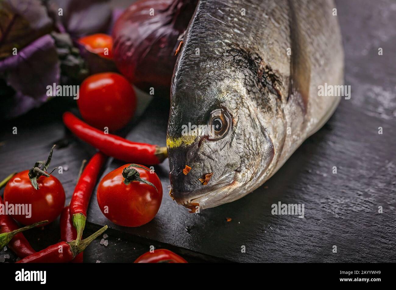 Fresh raw dorado. Fish, spices, chili peppers, salt, onions, tomatoes and basil on a dark wooden table. Close up. Sea food Stock Photo