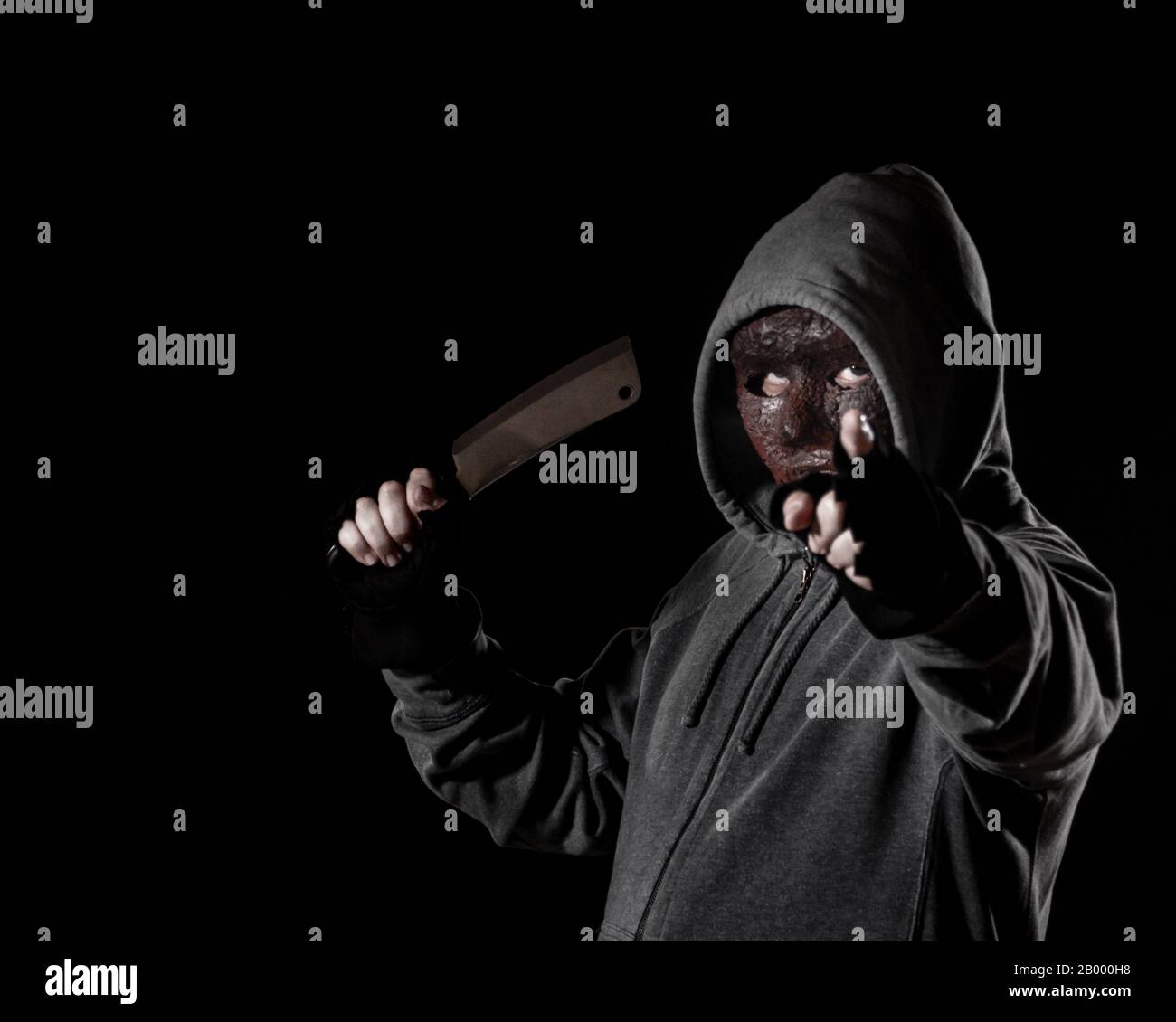 Scary killer in mask and hoodie holding knife and pointing finger Stock Photo