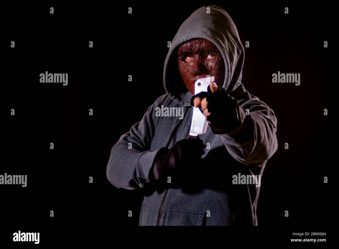 Scary killer in mask and hoodie holding knife and pointing finger Stock Photo