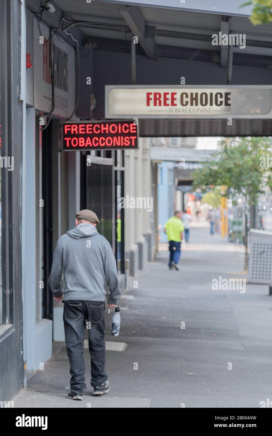 An older man in a hoodie and flat cap or hat walks near a Free Choice Tobacconist shop of tobacco store in the Melbourne suburb of Fitzroy, Australia Stock Photo