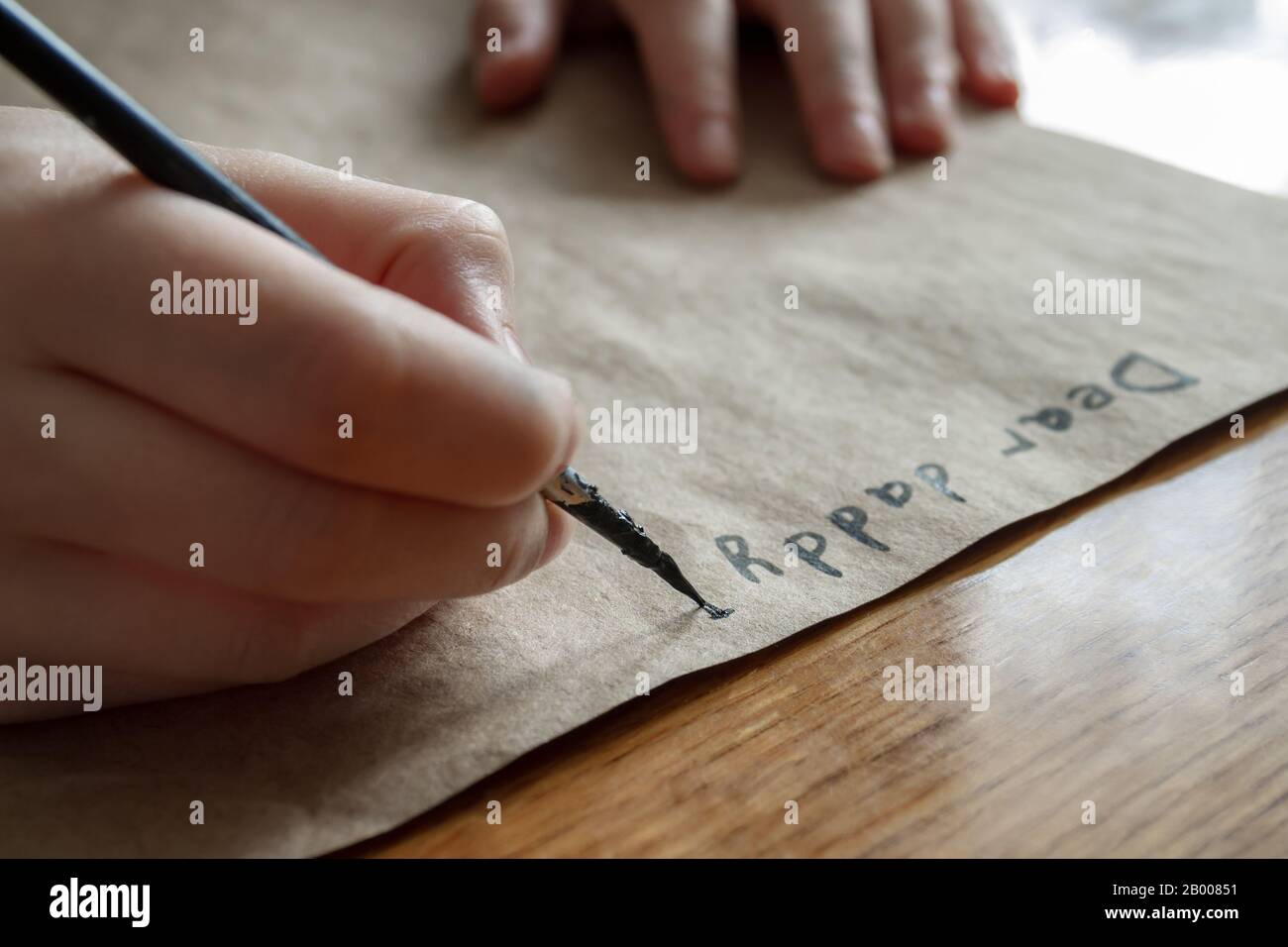 A small girl writes a letter to dear daddy by black paint on brown