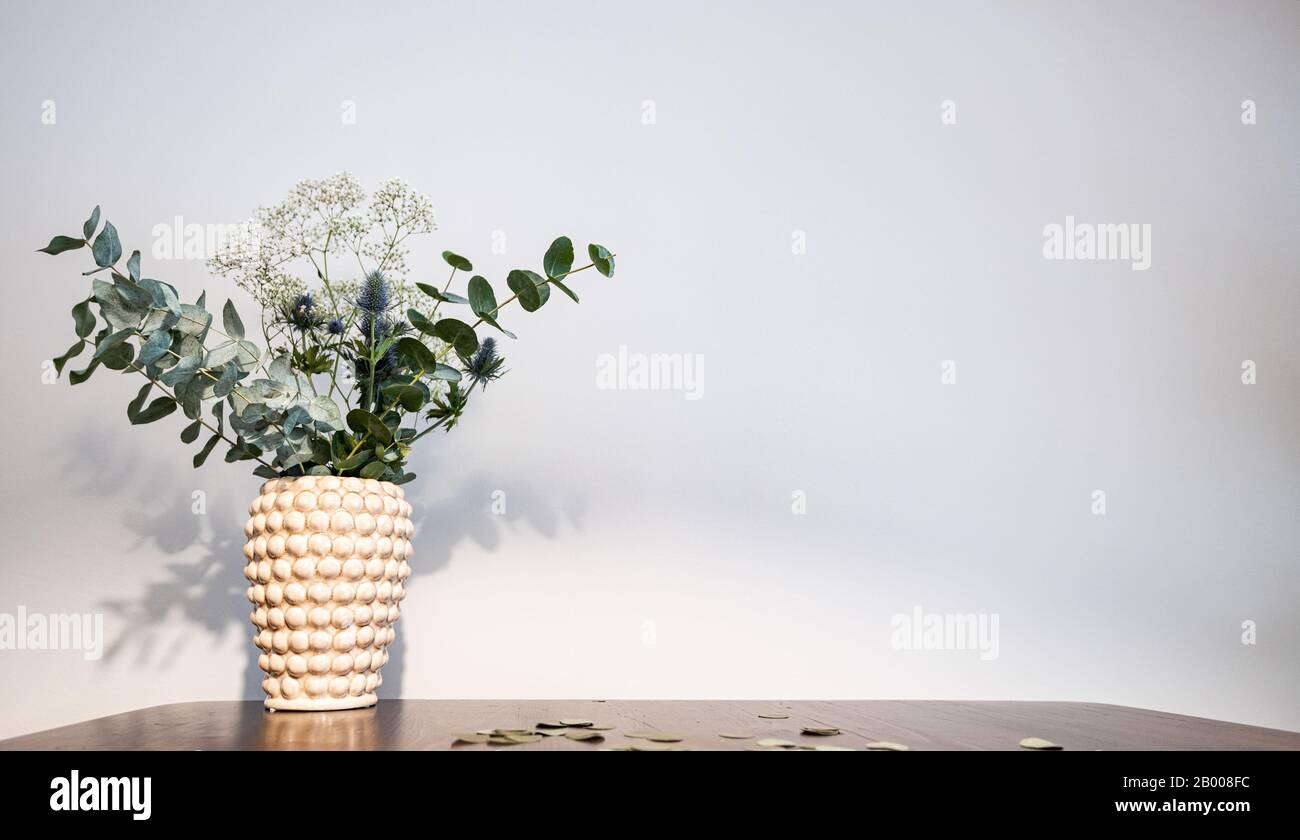 Vase with a bouquet of white and blue flowers on a wooden table before a grey background. golden confetti lying on the table. Stock Photo