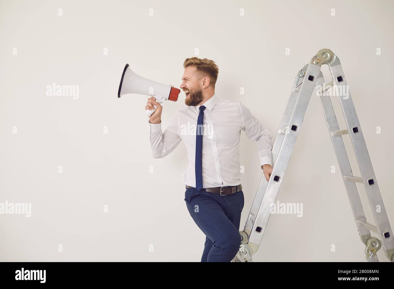 A bearded businessman on the stairs with a megaphone in hand shouts Stock Photo