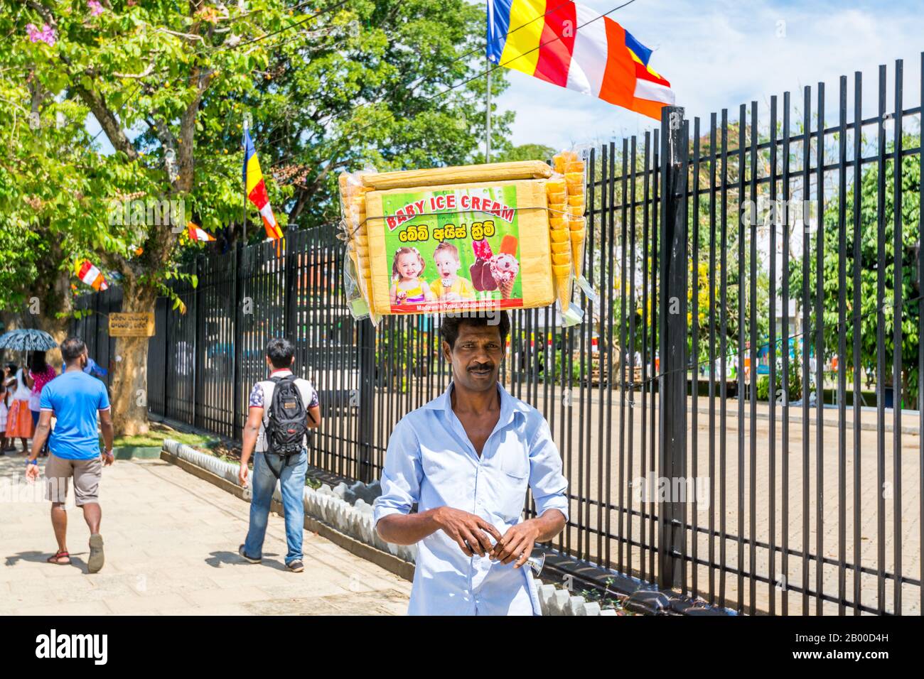 A man with a basket full of icecream on the head walking outside of the shrine of Sri Dalada Maligawa or the Temple of the Sacred Tooth Relic, in Kand Stock Photo