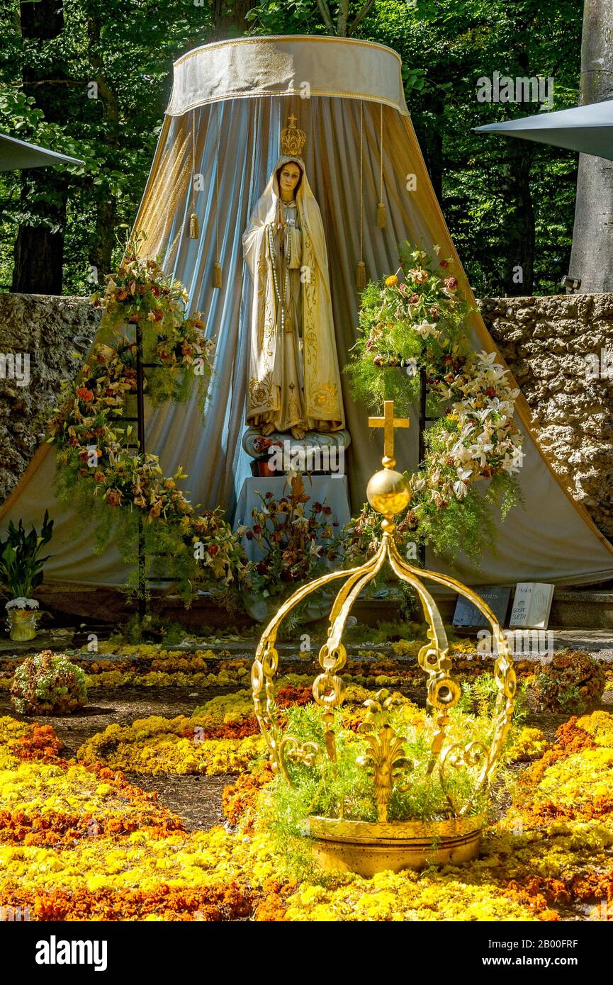 Statue of the Madonna, carpet of flowers with golden crown of the Virgin Mary, grotto of the Virgin Mary in the forest, pilgrimage place Maria Stock Photo
