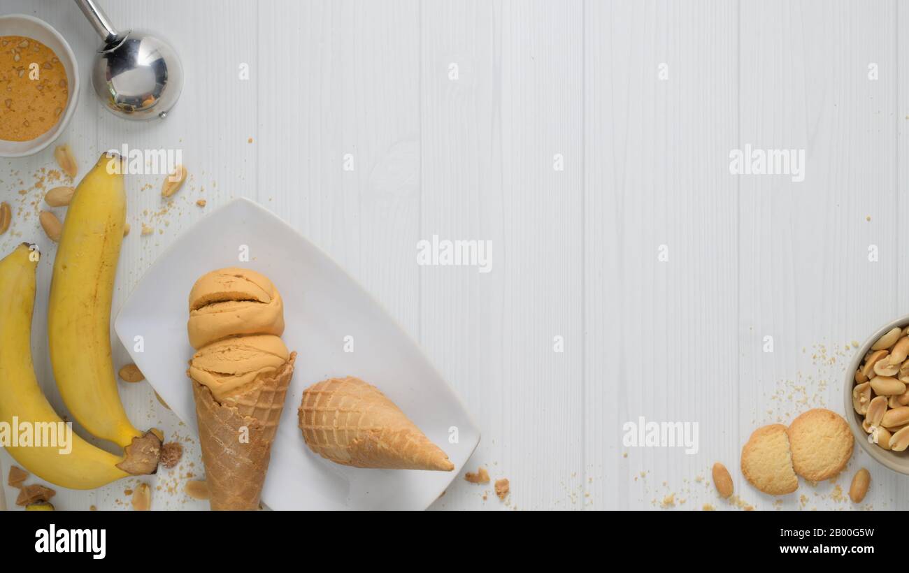 Top view of summer dessert with peanut butter banana flavour ice-cream cones, topping and copy space on plank desk background Stock Photo