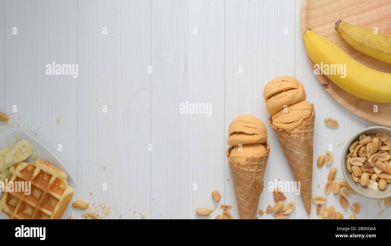 Top view of summer dessert with peanut butter banana flavour ice-cream cones, waffle, topping and copy space on plank desk background Stock Photo