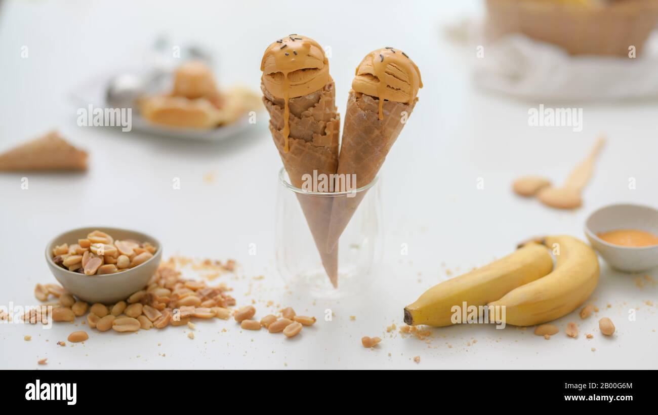 Close up view of summer dessert with peanut butter banana flavour ice-cream cones, topping and copy space on white desk background Stock Photo