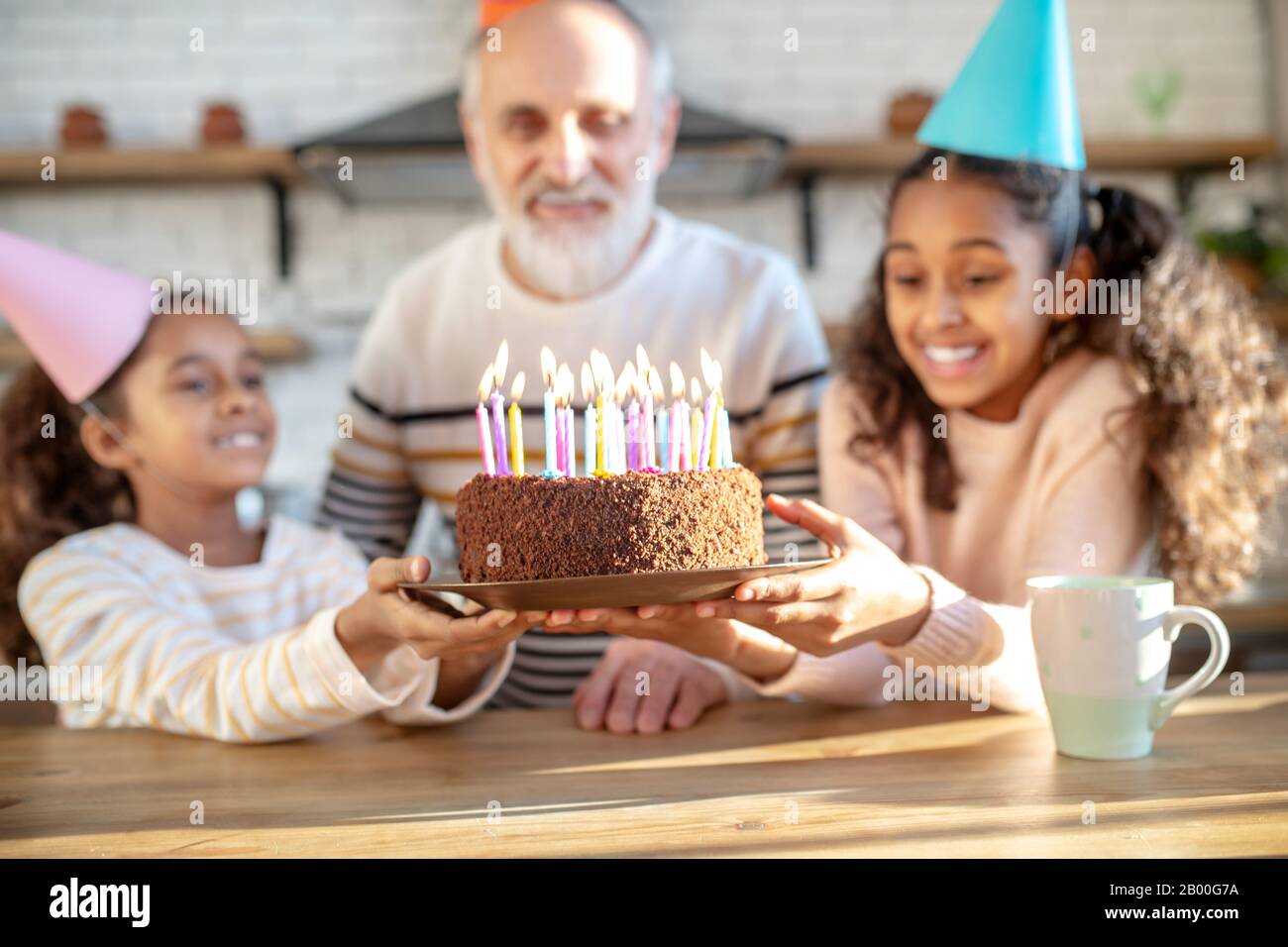 Two dark-skinned girls holding his grandads birthday cake Stock Photo