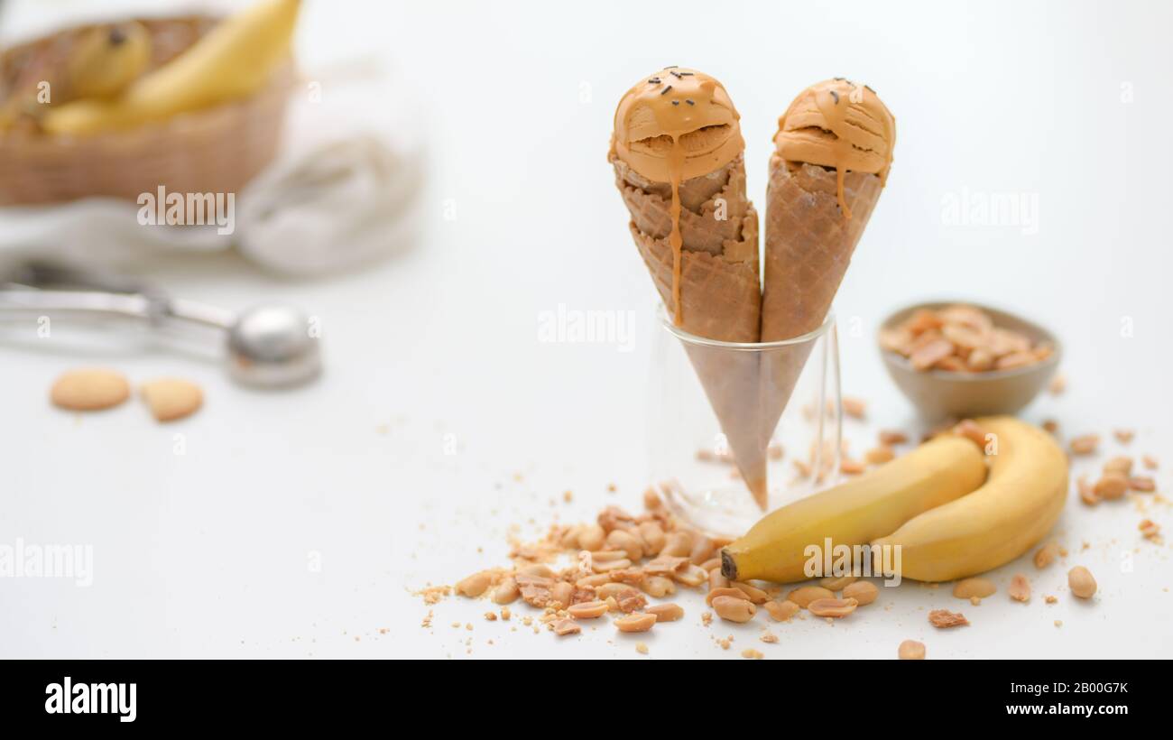 Cropped shot of summer dessert with peanut butter banana flavour ice-cream cones, topping and copy space on white table background Stock Photo