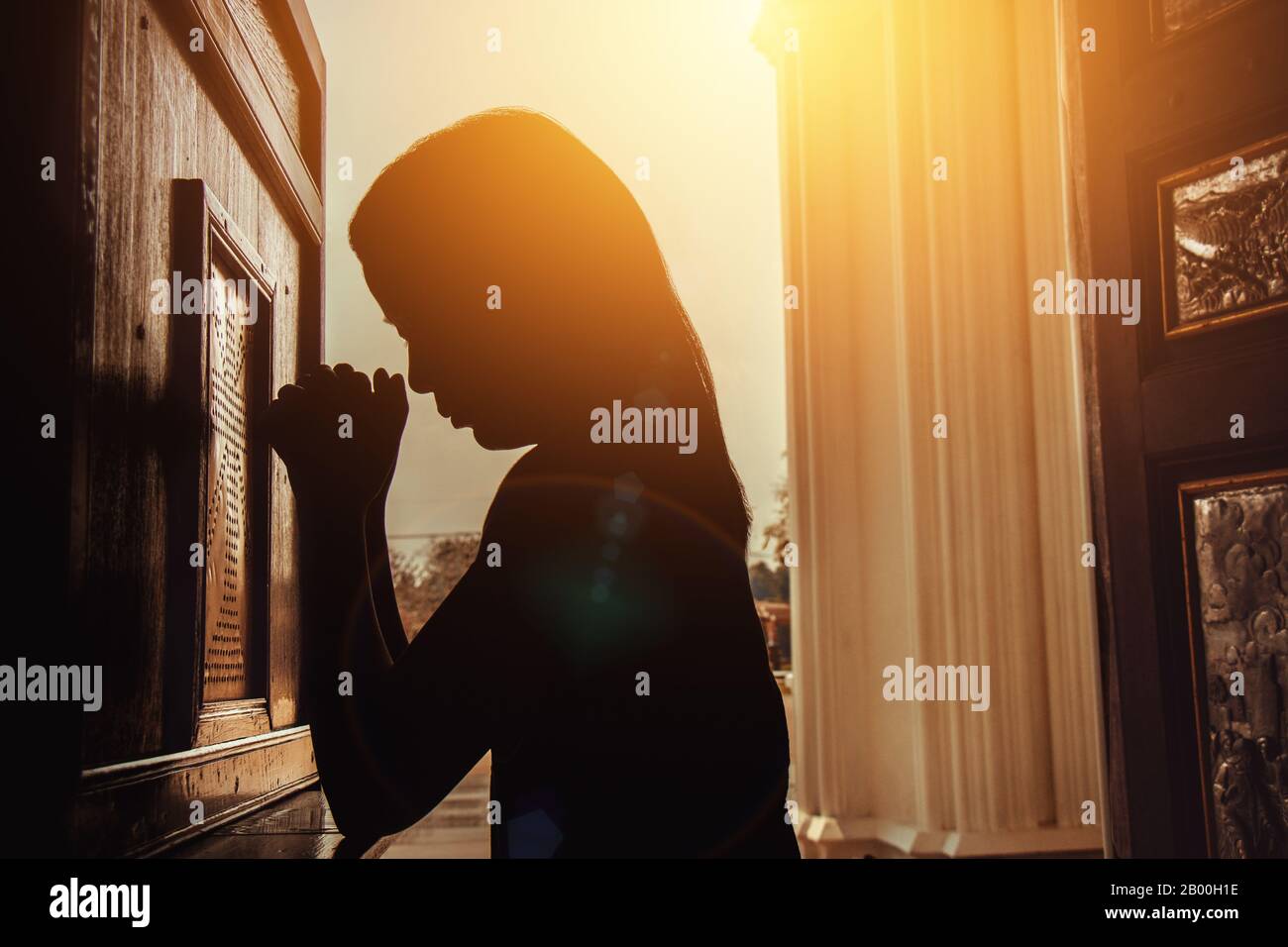 silhouette of woman kneeling and praying in modern church at sunset time Stock Photo