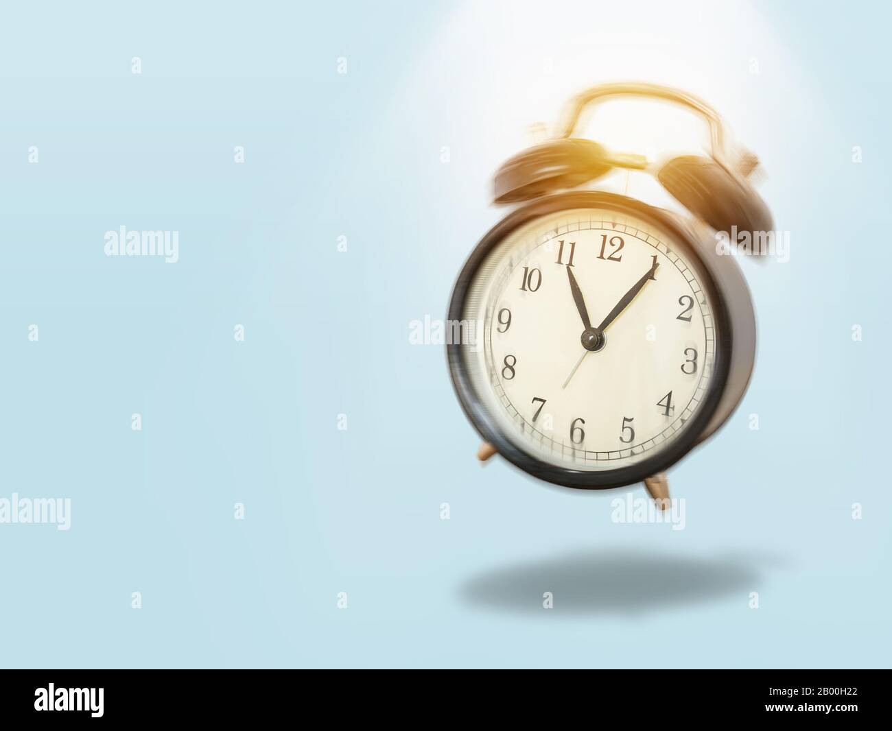 black vintage alarm clock with movement shaking and make a noise in the morning with lighting shine on top. black alarm clock isolated on blue bg Stock Photo