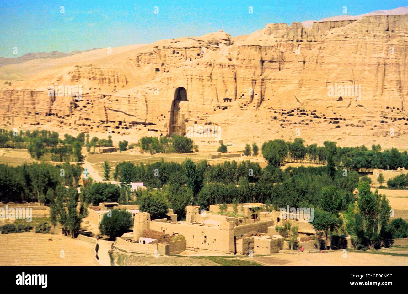 Afghanistan: Vale of Bamiyan in 1979, with the larger of the two Bamiyan Buddhas left centre. Photo by Andrew Forbes.  The Buddhas of Bamiyan were two 6th century monumental statues of standing buddhas carved into the side of a cliff in the Bamiyan valley in the Hazarajat region of central Afghanistan, situated 230 km (143 miles) northwest of Kabul at an altitude of 2,500 meters (8,202 ft).  Built in 507 CE, the larger in 554 CE, the statues represented the classic blended style of Gandhara art. The main bodies were hewn directly from the sandstone cliffs. Stock Photo