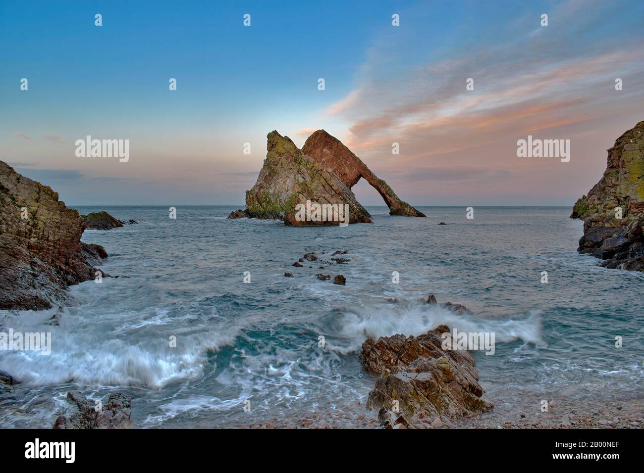 BOW FIDDLE ROCK PORTKNOCKIE MORAY FIRTH SCOTLAND WINTER PINK CLOUD SUNSET WITH WAVES BREAKING ON ROCKS AND PEBBLE BEACH Stock Photo