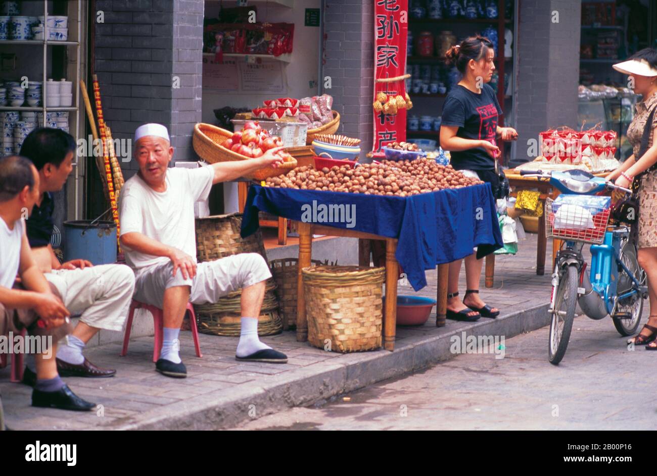 China: A Hui walnut vendor points the way on a busy street in Xi'an's Muslim Quarter, Shaanxi Province.  Xi'an is the capital of Shaanxi province, and a sub-provincial city in the People's Republic of China. One of the oldest cities in China, with more than 3,100 years of history, the city was known as Chang'an before the Ming Dynasty.  Xi'an is one of the Four Great Ancient Capitals of China, having held that position under several of the most important dynasties in Chinese history, including the Zhou, Qin, Han, Sui, and Tang. Xi'an is the eastern terminus of the Silk Road. Stock Photo