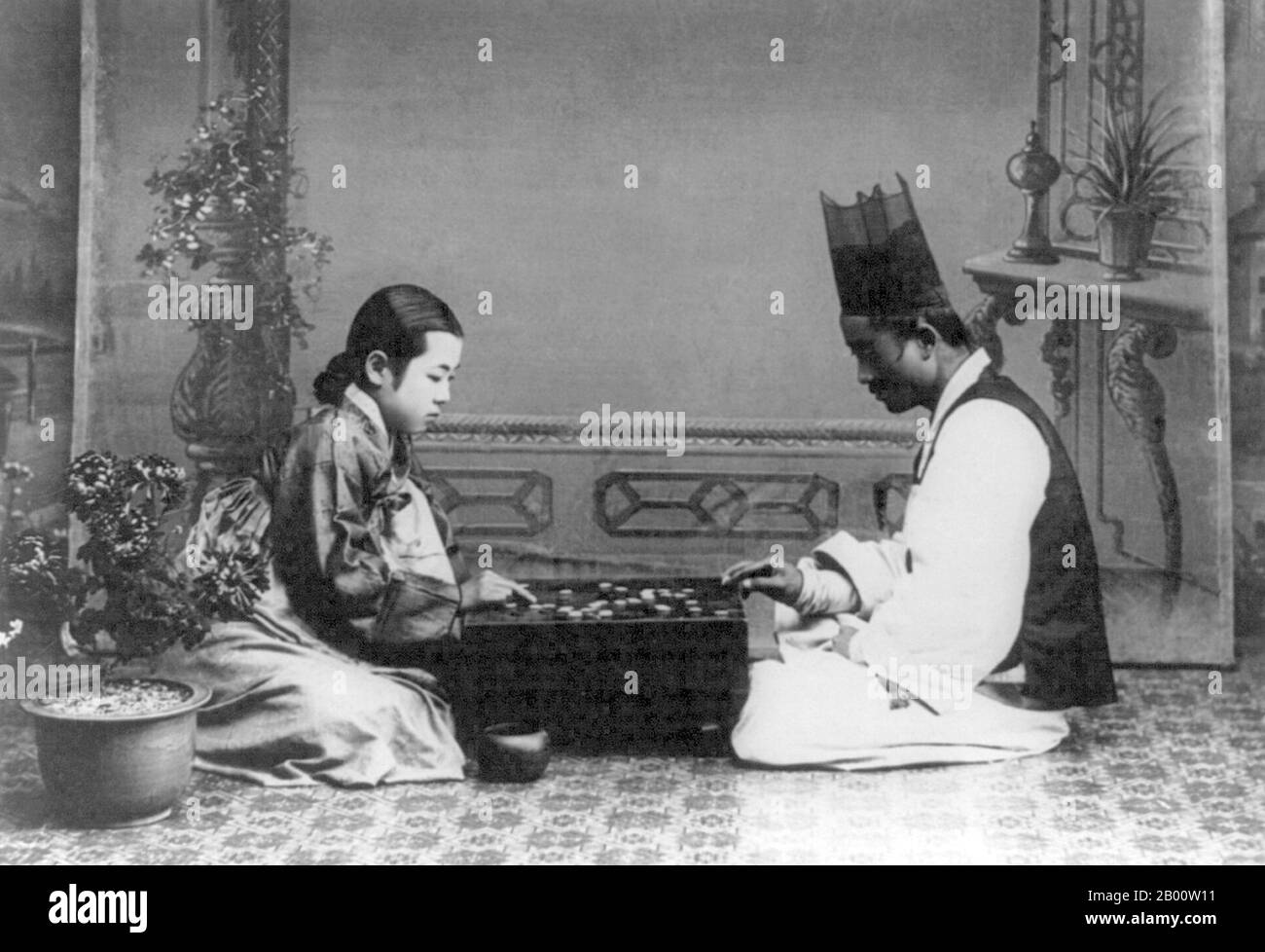 Korea: A man and a woman playing a game of 'baduk' or 'go', c. 1910.  Go (Japanese), known as 'weiqi' in Chinese and 'baduk' in Korean, is an ancient board game for two players that is noted for being rich in strategy despite its relatively simple rules. Stock Photo