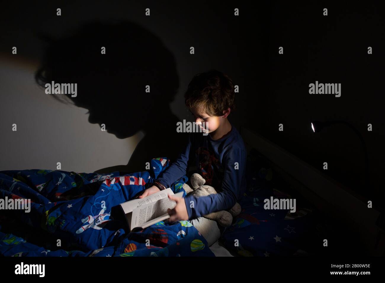 6 year old boy reading an Enid Blyton book at night time in his bedroom, England, United Kingdom Stock Photo