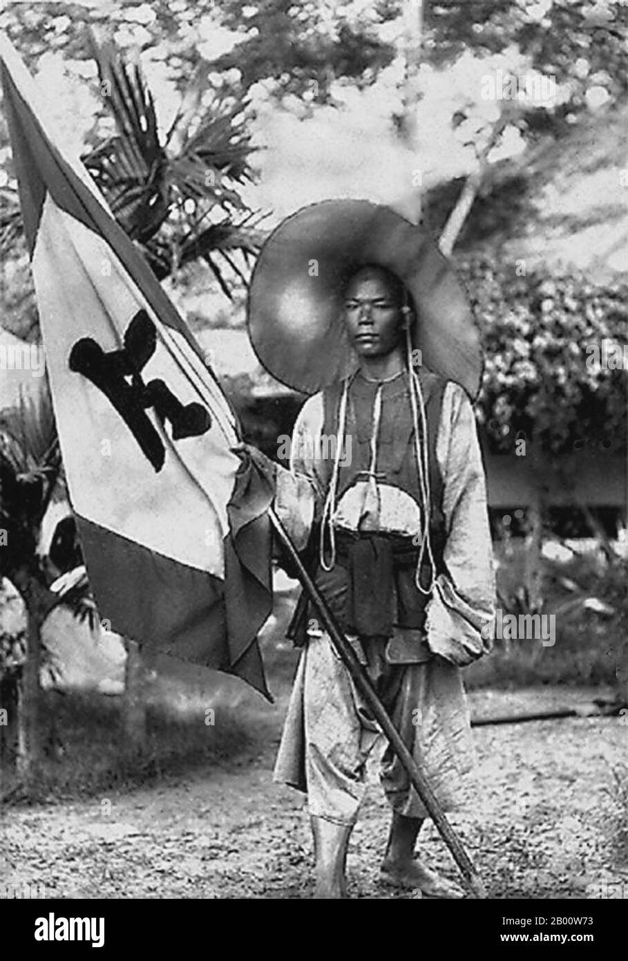 Vietnam: A Black Flag soldier with the Black Flag banner, Tonkin. Photo by Charles-Edouard Hocquard (1853-1911), 1885.  The Black Flag Army (Chinese: Heiqi Jun) was a remnant of a bandit group who may have been former Taiping rebels that crossed the border from Guangxi province of China into Upper Tonkin, in the Empire of Annam (Vietnam) in 1865. They became known mainly for their fights against French forces in cooperation with both Vietnamese and Chinese authorities. The Black Flag Army is so named because of the preference of its commander, Liu Yongfu, for using black command flags. Stock Photo