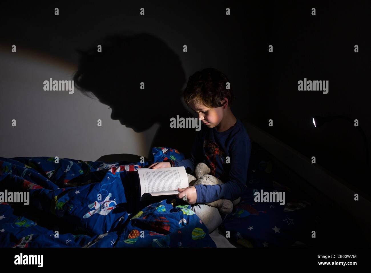 6 year old boy reading an Enid Blyton book at night time in his bedroom, England, United Kingdom Stock Photo