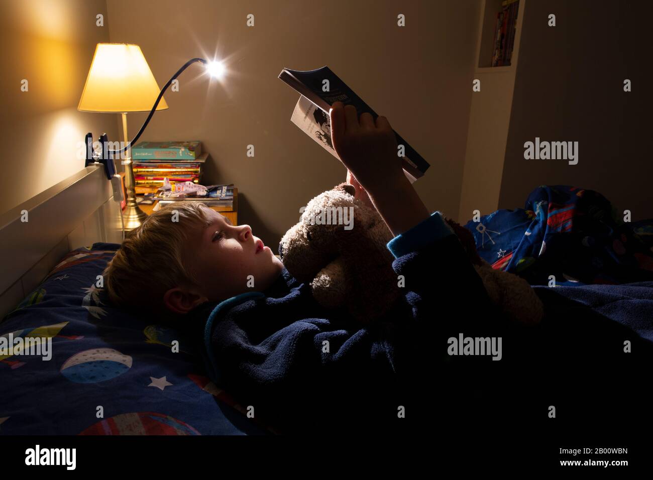 9 year old boy reading an Enid Blyton book at night time in his bedroom, England, United Kingdom Stock Photo