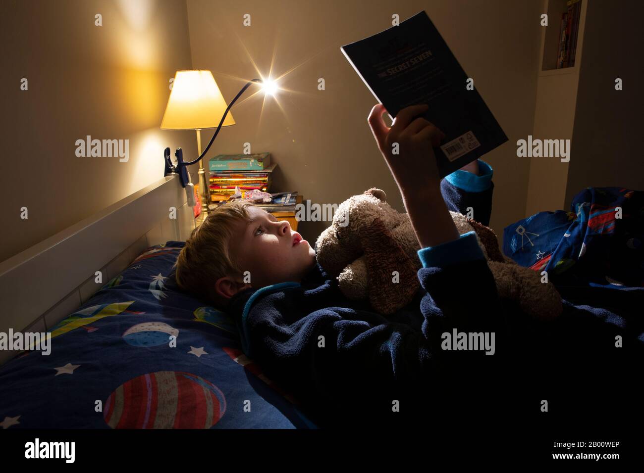 9-year-old boy reading an Enid Blyton book at night time in his bedroom, England, United Kingdom Stock Photo