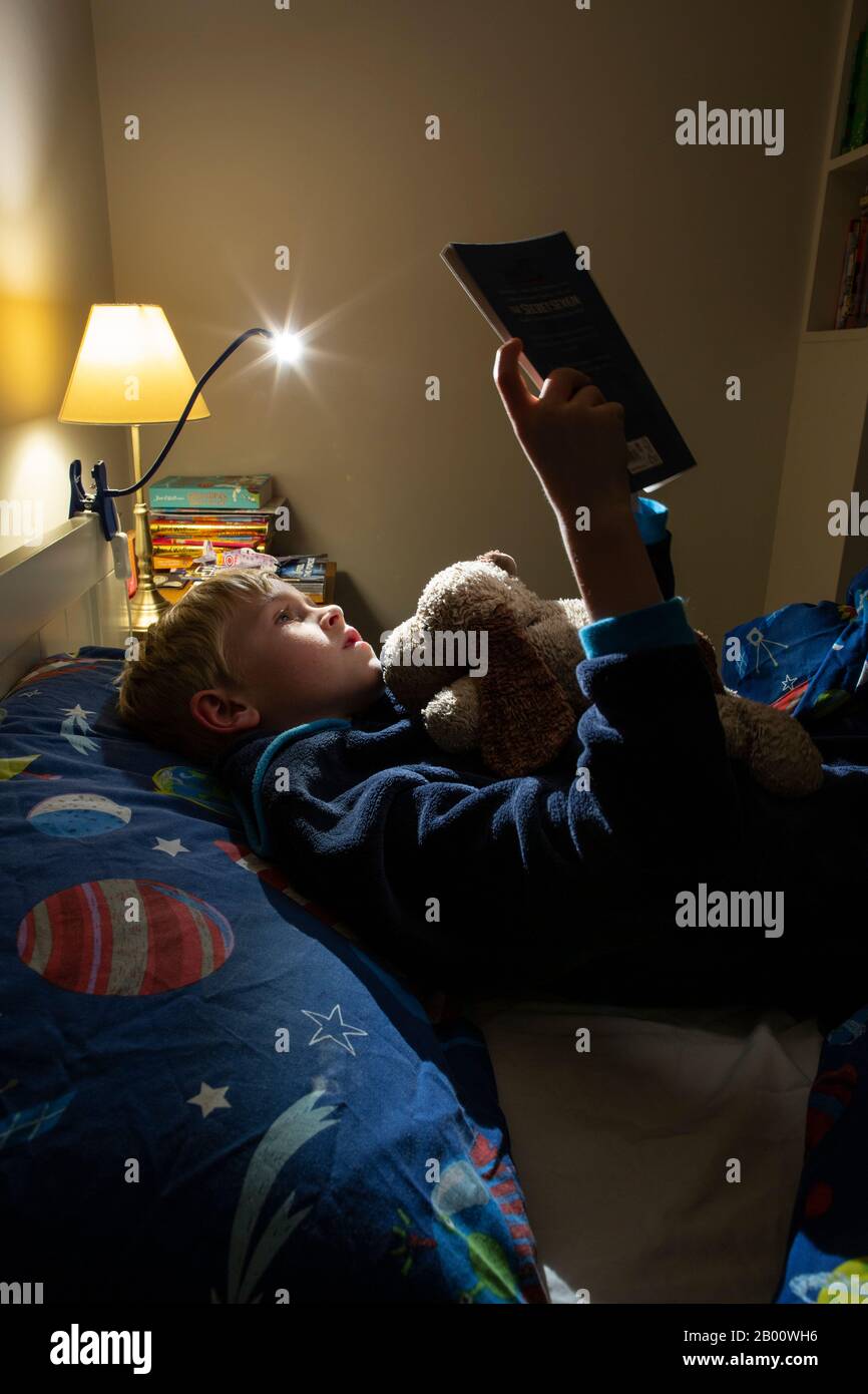 9 year old boy reading an Enid Blyton book at night time in his bedroom, England, United Kingdom Stock Photo
