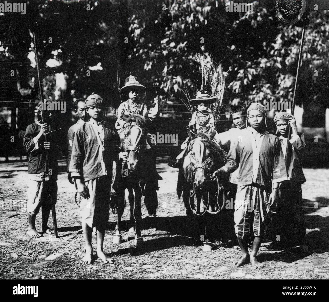 Laos: Two of HM Sisavang Vong’s many children take a ride on horses with servants in attendance, photographed in 1919.  Sisavang Phoulivong (1885 - 1959) was the king of Luang Prabang and later the Kingdom of Laos. His father was king Zakarine and his mother was Queen Thongsy. He was educated at Lycée Chasseloup-Laubat, Saigon, and at l'École Coloniale in Paris. He was known as a 'playboy' king with up to 50 children by as many as 15 wives. Stock Photo