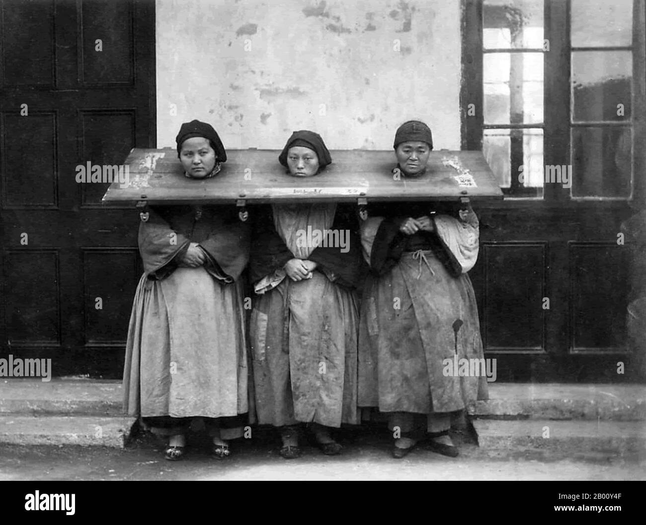 China: Three women wearing a cangue or form of portable stocks as a punishment, c. 1900.  A cangue was a device that was used for public humiliation and corporal punishment in China and some other parts of East Asia and Southeast Asia until the early years of the 20th century. It was somewhat similar to the pillory used for punishment in the West, except that the board of the cangue was not fixed to a base, and had to be carried around by the prisoner. Stock Photo
