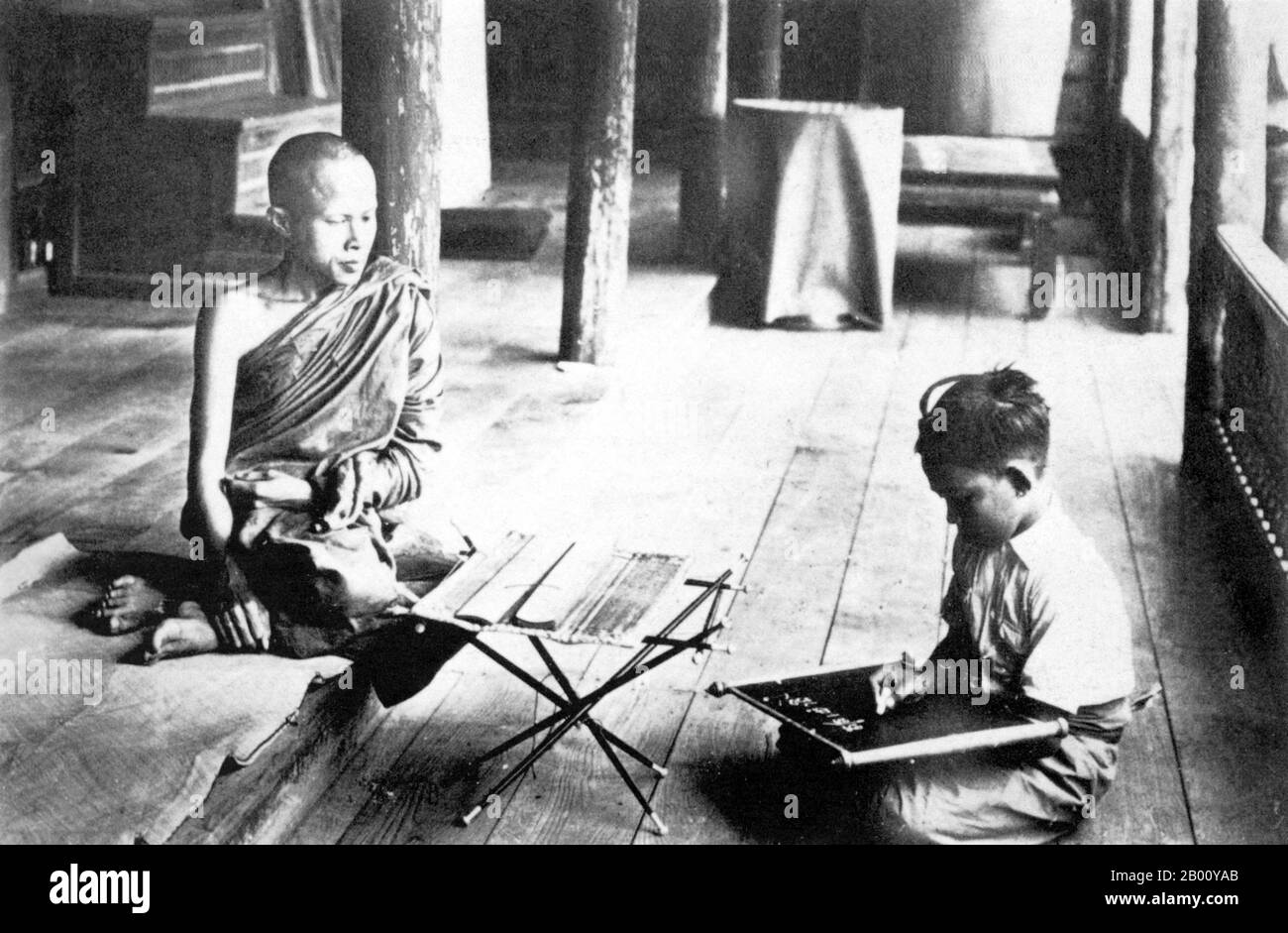 Thailand: A 1900 photograph of a Buddhist monk teaching a child in Nakhon Phanom in Isarn, northeastern Siam.  Nakhon Phanom, once the center of the ancient Sri Kotrabun Kingdom, lies adjacent to the Mekong River, 735 kms northeast of Bangkok. The area was long settled by ethnic Lao people and belonged to the Lan Xang Kingdom even after it came under the control of Ayutthaya. At first it was known as 'Si Kotrabun', and during the times of King Rama I as 'Maruka Nakhon'. Stock Photo