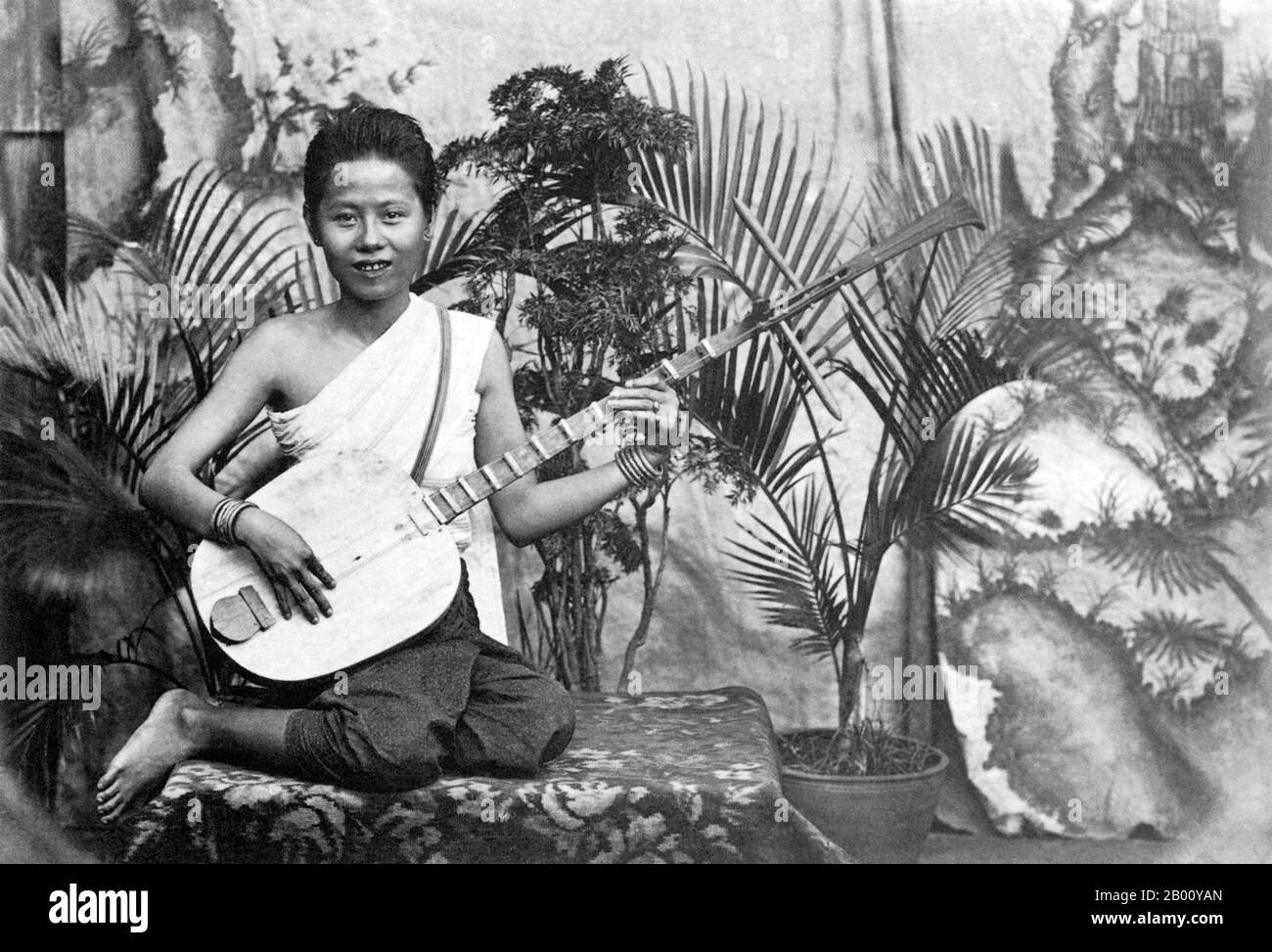 Cambodia: A 1928 photograph of a young musician playing a 'chapei' in the Royal Palace in Phnom Penh.  A 'chapei dong veng' is a Khmer two-stringed, long-necked traditional guitar. The girl in the picture would most likely have played to the court of King Sisowath Monivong who was the king of Cambodia from 1927 until 1941. Stock Photo