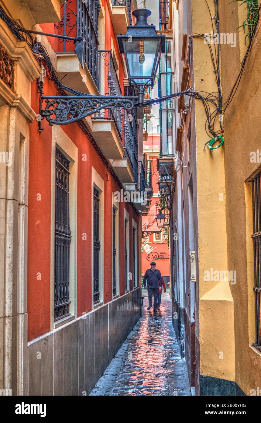 Narrow street in the Barrio Santa Cruz with people walking. Wet pavement.  Typical colors in the buildings. Stock Photo