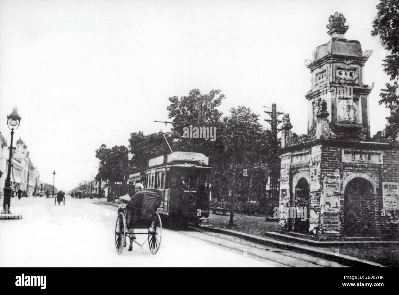 Vietnam: A rickshaw and an electric tram pass Hoa Phong Tower, near Hoan Kiem Lake in Hanoi (early 20th century).  Hoa Phong Tower is the last remaining relic of Bao An pagoda, which was a famous Buddhist site in the 19th century in Hanoi. The pagoda was built in 1846 with four dates in the style of an Indian stupa under the command of Nguyen Dang Giai. The pagoda was destroyed in 1898 to broaden the street and only the tower was left standing. Today the tower stands opposite the main post office on the bank of Hoan Kiem Lake. Stock Photo