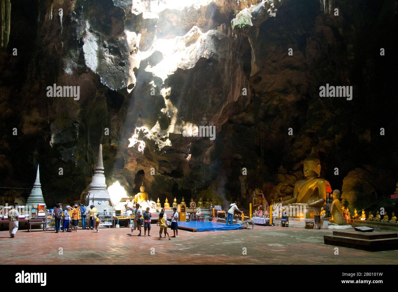 Thailand: Worshippers inside the main cavern at Tham Khao Luang, Phetchaburi.  Tham Khao Luang is a large cave consisting of three linked chambers and is distinguished by many hanging stalactites and Buddha images, including a phra non or reclining Buddha. The main bronze image was cast on the orders of King Chulalongkorn (Rama V) and dedicated to his illustrious predecessors, Kings Rama III and Rama IV. There is a natural opening in the ceiling of the second, main chamber, through which daylight streams illuminating the images within. Stock Photo